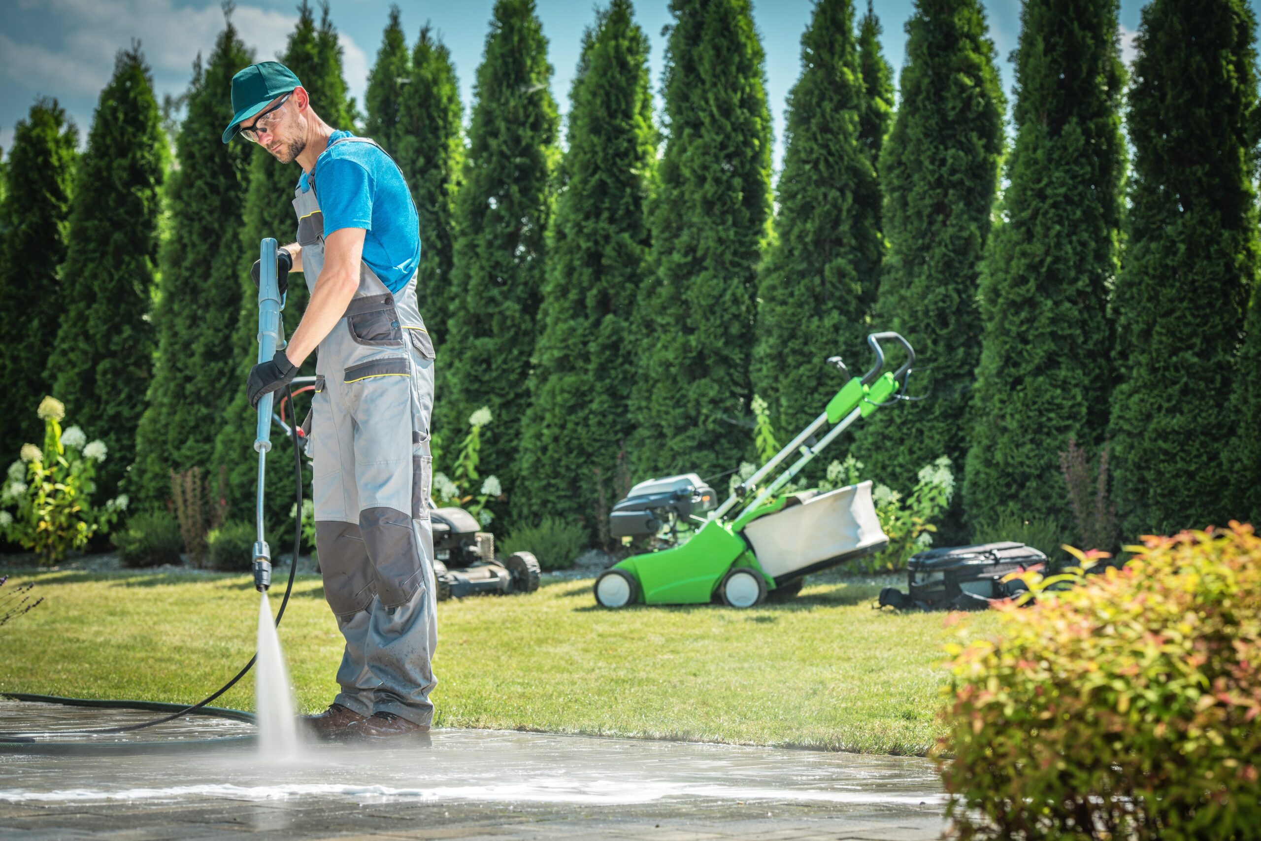 Mann reinigt Gartenwege und Auffahrt mit professionellem Hochdruckreiniger. Gartengeräte im Hintergrund.